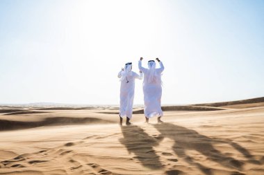 Çölde geleneksel emirati Arap kandurası giyen iki ortadoğulu Müslüman arkadaş Dubai 'deki kum tepelerinde buluşuyor.