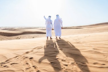 Çölde geleneksel emirati Arap kandurası giyen iki ortadoğulu Müslüman arkadaş Dubai 'deki kum tepelerinde buluşuyor.
