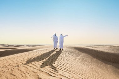 Çölde geleneksel emirati Arap kandurası giyen iki ortadoğulu Müslüman arkadaş Dubai 'deki kum tepelerinde buluşuyor.