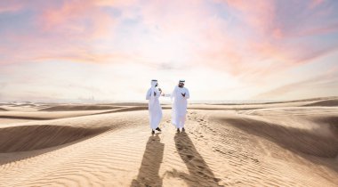 Çölde geleneksel emirati Arap kandurası giyen iki ortadoğulu Müslüman arkadaş Dubai 'deki kum tepelerinde buluşuyor.