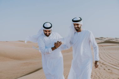 Çölde geleneksel emirati Arap kandurası giyen iki ortadoğulu Müslüman arkadaş Dubai 'deki kum tepelerinde buluşuyor.