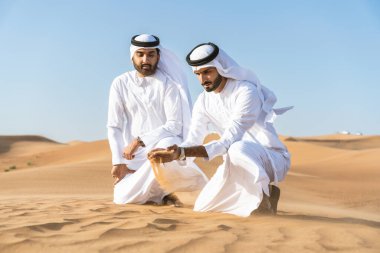 Çölde geleneksel emirati Arap kandurası giyen iki ortadoğulu Müslüman arkadaş Dubai 'deki kum tepelerinde buluşuyor.