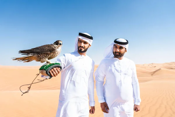 两名中东男子穿着传统的亚拉提亚拉布 坎杜拉头巾 与猎鹰 阿拉伯穆斯林朋友在迪拜沙丘相遇 — 图库照片