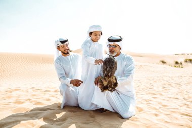 Dubai çölünde safari yapan üç nesillik bir aile. Büyükbaba, oğul ve torun doğada birlikte vakit geçirip şahin kuşlarını eğitiyorlar..
