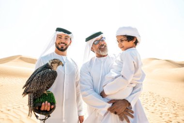 Dubai çölünde safari yapan üç nesillik bir aile. Büyükbaba, oğul ve torun doğada birlikte vakit geçirip şahin kuşlarını eğitiyorlar..