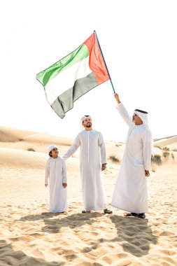 Dubai çölünde beyaz kandura kıyafeti içinde safari yapan üç kuşak aile. Büyükbaba, oğul ve torun doğada birlikte vakit geçiriyorlar..