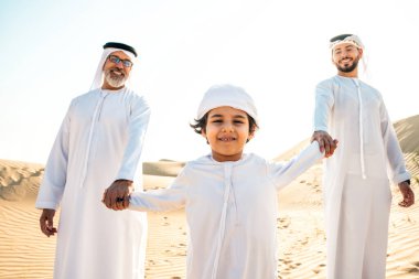Dubai çölünde beyaz kandura kıyafeti içinde safari yapan üç kuşak aile. Büyükbaba, oğul ve torun doğada birlikte vakit geçiriyorlar..