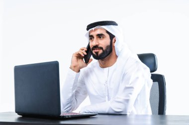 Dubai 'de çalışan Kandora giyen orta doğulu bir iş adamı, bilgisayar masasında oturan ve uzaktan kumandayla çalışan yakışıklı bir iş adamı.