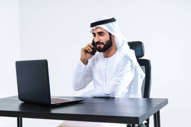 Dubai 'de çalışan Kandora giyen orta doğulu bir iş adamı, bilgisayar masasında oturan ve uzaktan kumandayla çalışan yakışıklı bir iş adamı.