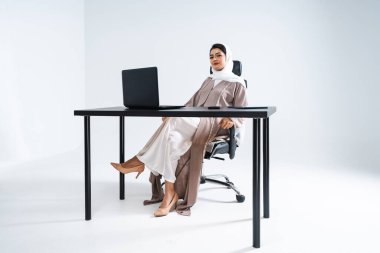 Arap, ortadoğulu, geleneksel abaya elbisesiyle iş kadını Dubai, Birleşik Arap Emirlikleri 'ndeki bilgisayar masasında çalışan Müslüman kadın portresi.