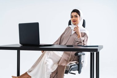 Arap, ortadoğulu, geleneksel abaya elbisesiyle iş kadını Dubai, Birleşik Arap Emirlikleri 'ndeki bilgisayar masasında çalışan Müslüman kadın portresi.