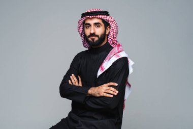 Stüdyoda geleneksel Suudi kıyafetleri olan yakışıklı Arap orta doğulu adam - Arap Müslüman yetişkin iş adamı beyaz arka planda izole edilmiş thwab portresi takıyor.