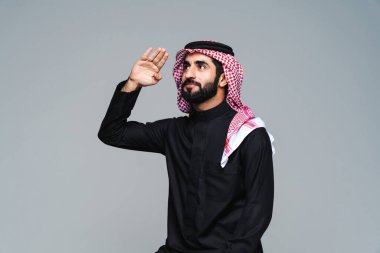 Stüdyoda geleneksel Suudi kıyafetleri olan yakışıklı Arap orta doğulu adam - Arap Müslüman yetişkin iş adamı beyaz arka planda izole edilmiş thwab portresi takıyor.