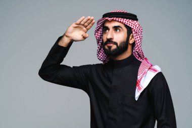 Stüdyoda geleneksel Suudi kıyafetleri olan yakışıklı Arap orta doğulu adam - Arap Müslüman yetişkin iş adamı beyaz arka planda izole edilmiş thwab portresi takıyor.