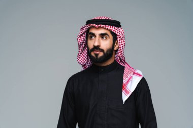 Stüdyoda geleneksel Suudi kıyafetleri olan yakışıklı Arap orta doğulu adam - Arap Müslüman yetişkin iş adamı beyaz arka planda izole edilmiş thwab portresi takıyor.