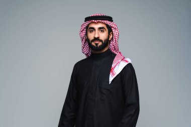 Stüdyoda geleneksel Suudi kıyafetleri olan yakışıklı Arap orta doğulu adam - Arap Müslüman yetişkin iş adamı beyaz arka planda izole edilmiş thwab portresi takıyor.