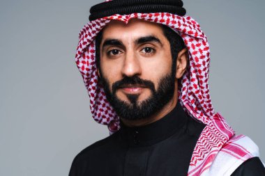 Stüdyoda geleneksel Suudi kıyafetleri olan yakışıklı Arap orta doğulu adam - Arap Müslüman yetişkin iş adamı beyaz arka planda izole edilmiş thwab portresi takıyor.