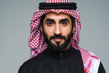 Stüdyoda geleneksel Suudi kıyafetleri olan yakışıklı Arap orta doğulu adam - Arap Müslüman yetişkin iş adamı beyaz arka planda izole edilmiş thwab portresi takıyor.
