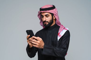 Stüdyoda geleneksel Suudi kıyafetleri olan yakışıklı Arap orta doğulu adam - Arap Müslüman yetişkin iş adamı beyaz arka planda izole edilmiş thwab portresi takıyor.