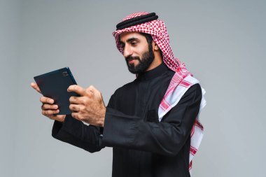 Stüdyoda geleneksel Suudi kıyafetleri olan yakışıklı Arap orta doğulu adam - Arap Müslüman yetişkin iş adamı beyaz arka planda izole edilmiş thwab portresi takıyor.