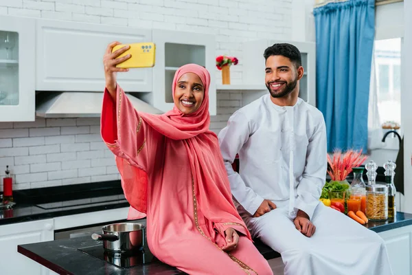 Happy middle-eastern couple wearing traditional arab clothing at home - Married arabian husband and wife bonding together in the apartment, concepts about relationship, domestic life and emirati lifestyle