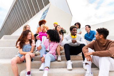 Açık havada kaynaşan neşeli çoklu etnik kökenli genç arkadaş grubu - çok ırklı öğrenciler şehirde buluşuyor, gençlik kavramları, insan yaşam tarzı, çeşitlilik, gençlik ve şehir hayatı