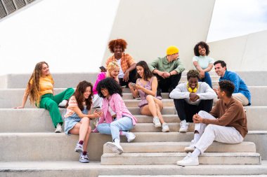 Açık havada kaynaşan neşeli çoklu etnik kökenli genç arkadaş grubu - çok ırklı öğrenciler şehirde buluşuyor, gençlik kavramları, insan yaşam tarzı, çeşitlilik, gençlik ve şehir hayatı