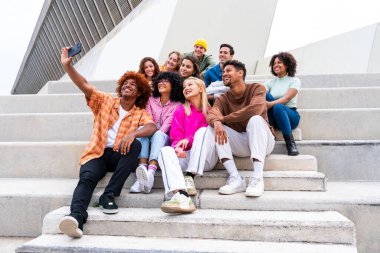 Açık havada kaynaşan neşeli çoklu etnik kökenli genç arkadaş grubu - çok ırklı öğrenciler şehirde buluşuyor, gençlik kavramları, insan yaşam tarzı, çeşitlilik, gençlik ve şehir hayatı