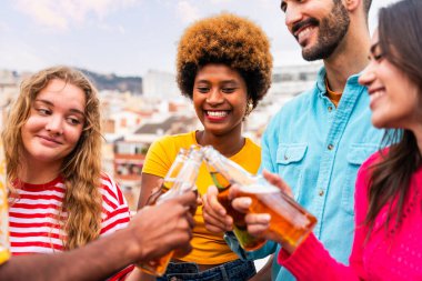 Çok ırklı bir grup mutlu genç arkadaş evlerinin çatısında barbekü partisi veriyorlar - çok ırklı neşeli genç insanlar teras balkonunda eğleniyor ve kaynaşıyorlar şehir manzarası ile, yiyip içiyorlar.