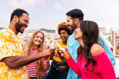 Çok ırklı bir grup mutlu genç arkadaş evlerinin çatısında barbekü partisi veriyorlar - çok ırklı neşeli genç insanlar teras balkonunda eğleniyor ve kaynaşıyorlar şehir manzarası ile, yiyip içiyorlar.