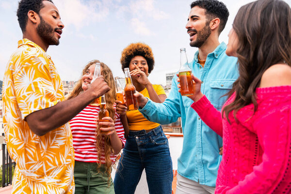 Multiethnic group of happy young friends having dinner barbecue party on rooftop at home - Multiracial cheerful young adult people having fun and bonding on a terrace balcony with city view, eating and drinking.
