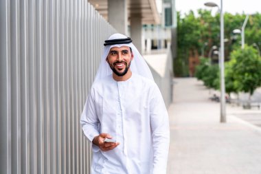 Arap Ortadoğu 'lu, Emirati Kandora giysili, şehirde geleneksel giysiler giyen Arap Müslüman iş adamı, şehir iş merkezinde geziniyor..