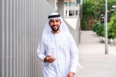 Arap Ortadoğu 'lu, Emirati Kandora giysili, şehirde geleneksel giysiler giyen Arap Müslüman iş adamı, şehir iş merkezinde geziniyor..
