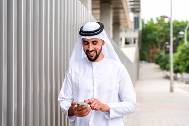 Arap Ortadoğu 'lu, Emirati Kandora giysili, şehirde geleneksel giysiler giyen Arap Müslüman iş adamı, şehir iş merkezinde geziniyor..