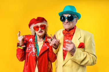Stüdyoda renkli arka planda rol yapan şık parti kıyafetleri giyen yaşlı ve güzel bir çift. Üçüncü yaş ve kıdem hakkında kavramsal imaj, yaşlı insanlar kendilerini genç hissediyorlar..