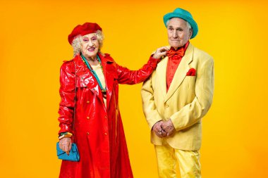 Stüdyoda renkli arka planda rol yapan şık parti kıyafetleri giyen yaşlı ve güzel bir çift. Üçüncü yaş ve kıdem hakkında kavramsal imaj, yaşlı insanlar kendilerini genç hissediyorlar..