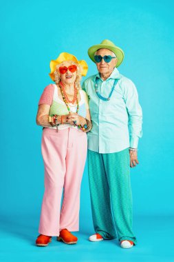 Stüdyoda renkli arka planda rol yapan şık parti kıyafetleri giyen yaşlı ve güzel bir çift. Üçüncü yaş ve kıdem hakkında kavramsal imaj, yaşlı insanlar kendilerini genç hissediyorlar..