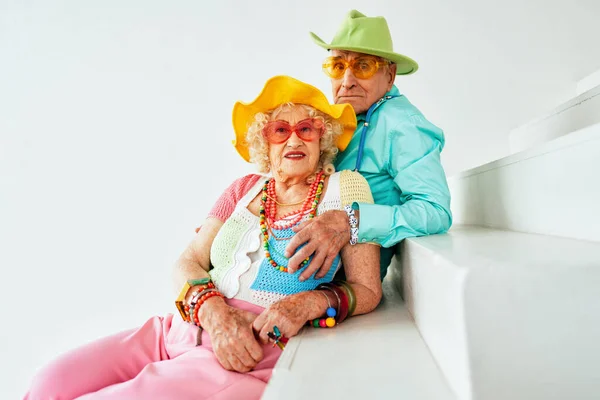 Beautiful senior old couple wearing fancy party clothes acting in studio on a colored background. Conceptual image about third age and seniority, old people feeling young inside.