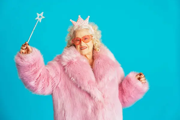 Beautiful senior old woman wearing fancy party clothes acting on a colored background in studio - Conceptual image about third age and seniority, old people feeling young inside.
