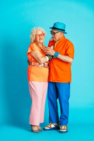 Beautiful senior old couple wearing fancy party clothes acting in studio on a colored background. Conceptual image about third age and seniority, old people feeling young inside.