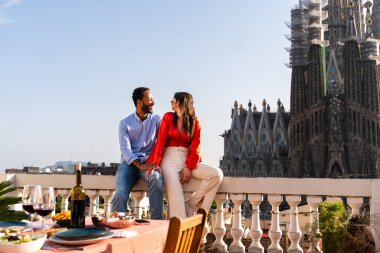 Sagrada Familia, Barcelona 'nın çatı katında buluşan çok ırklı, mutlu aşıklar şehir manzaralı bir terasta romantik aperatifler, turizm ve insan yaşam tarzı hakkında kavramlar