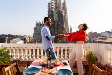 Sagrada Familia, Barcelona 'nın çatı katında buluşan çok ırklı, mutlu aşıklar şehir manzaralı bir terasta romantik aperatifler, turizm ve insan yaşam tarzı hakkında kavramlar
