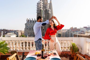 Sagrada Familia, Barcelona 'nın çatı katında buluşan çok ırklı, mutlu aşıklar şehir manzaralı bir terasta romantik aperatifler, turizm ve insan yaşam tarzı hakkında kavramlar