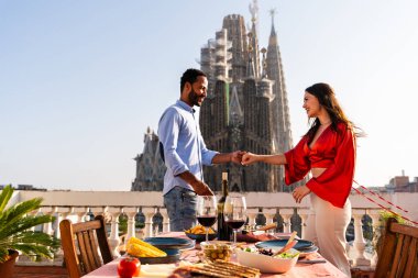 Sagrada Familia, Barcelona 'nın çatı katında buluşan çok ırklı, mutlu aşıklar şehir manzaralı bir terasta romantik aperatifler, turizm ve insan yaşam tarzı hakkında kavramlar