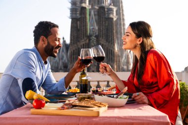 Sagrada Familia, Barcelona 'nın çatı katında buluşan çok ırklı, mutlu aşıklar şehir manzaralı bir terasta romantik aperatifler, turizm ve insan yaşam tarzı hakkında kavramlar