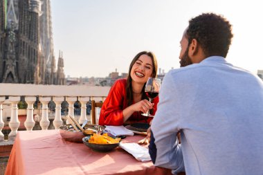 Sagrada Familia, Barcelona 'nın çatı katında buluşan çok ırklı, mutlu aşıklar şehir manzaralı bir terasta romantik aperatifler, turizm ve insan yaşam tarzı hakkında kavramlar