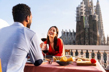 Sagrada Familia, Barcelona 'nın çatı katında buluşan çok ırklı, mutlu aşıklar şehir manzaralı bir terasta romantik aperatifler, turizm ve insan yaşam tarzı hakkında kavramlar