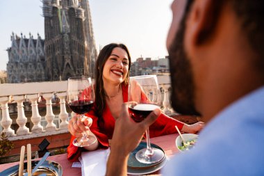 Sagrada Familia, Barcelona 'nın çatı katında buluşan çok ırklı, mutlu aşıklar şehir manzaralı bir terasta romantik aperatifler, turizm ve insan yaşam tarzı hakkında kavramlar