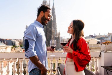 Sagrada Familia, Barcelona 'nın çatı katında buluşan çok ırklı, mutlu aşıklar şehir manzaralı bir terasta romantik aperatifler, turizm ve insan yaşam tarzı hakkında kavramlar