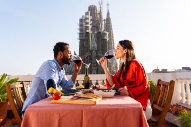 Sagrada Familia, Barcelona 'nın çatı katında buluşan çok ırklı, mutlu aşıklar şehir manzaralı bir terasta romantik aperatifler, turizm ve insan yaşam tarzı hakkında kavramlar